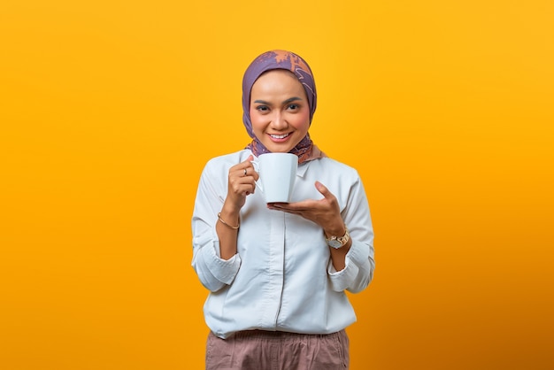 Portrait of beautiful Asian woman smiling and holding mug over yellow background