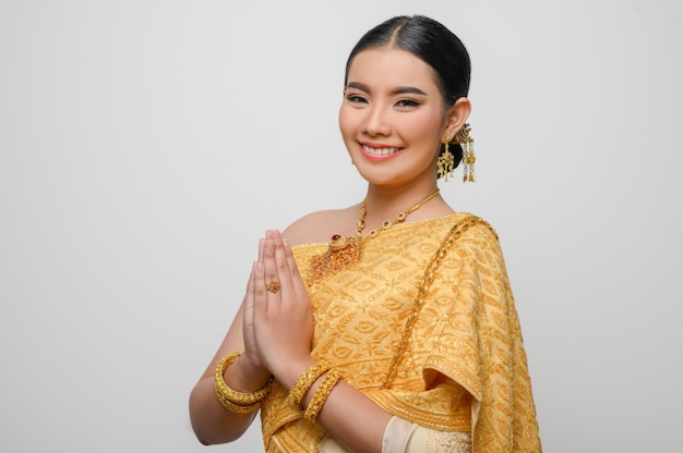 Portrait beautiful Asian woman in traditional Thai dress costume smile and pose raise hand with gracefully on white wall