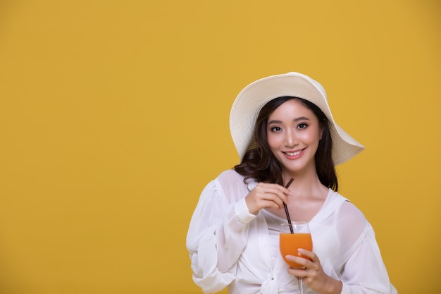 Portrait of beautiful Asian woman with hat holding a glass of orange juice