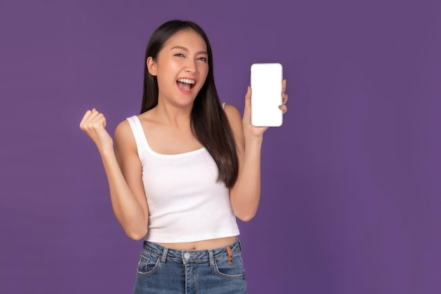 Portrait of beautiful Asian young woman showing smart phone with blank screen white screen empty copy space for advertising banner isolated on purple background Mock Up Image