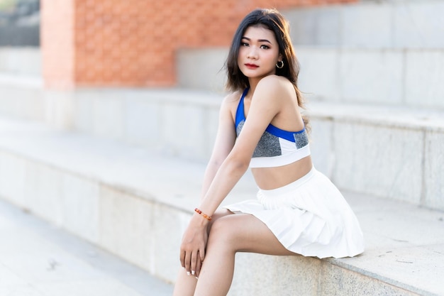 Portrait of beautiful athletic young asian woman in fashionable sportswear standing and having rest after strong exercise training in garden the parkOutdoor Sporty concept