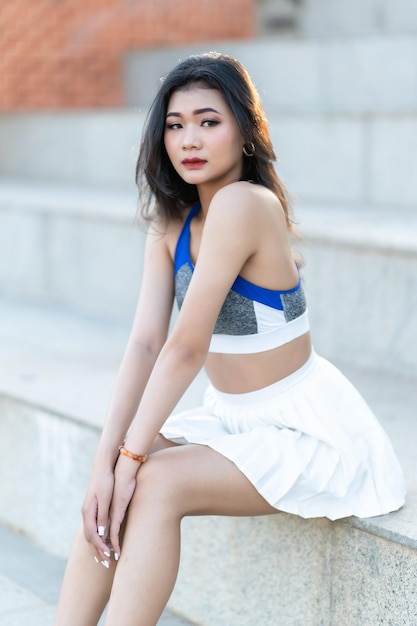 Portrait of beautiful athletic young asian woman in fashionable sportswear standing and having rest after strong exercise training in garden the parkOutdoor Sporty concept