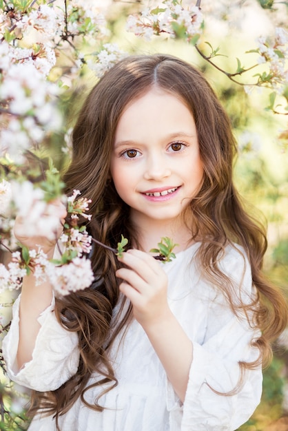 Portrait of a beautiful baby girl in a spring blooming garden. A girl on a background of white flowers.