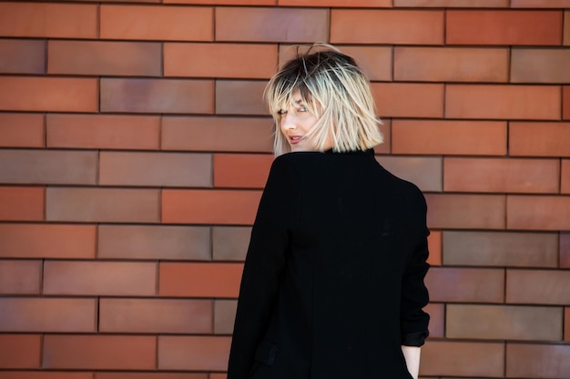 portrait of a beautiful blonde girl in a black jacket on a brick wall background