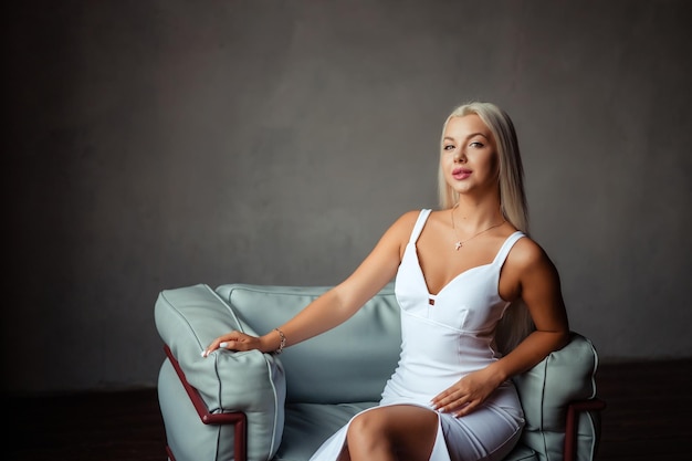 Portrait of a beautiful blonde girl in a white dress in the studio interior