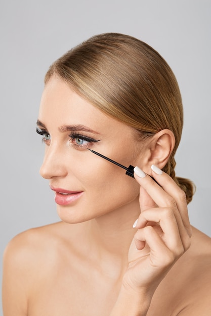 Portrait of beautiful blonde woman applying liquid eyeliner with brush. Natural make up.