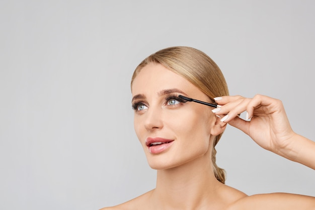 Portrait of beautiful blonde woman applying mascara with brush. Natural make up.Long lashes.