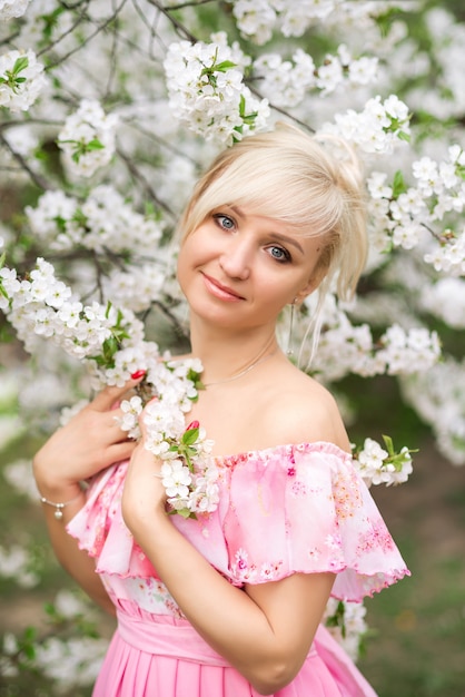 Portrait of a beautiful blonde woman in a pink dress in a blooming garden in spring.