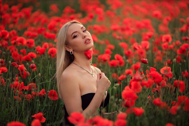 Portrait of a beautiful blonde woman in a straw hat at sunset on a poppy field