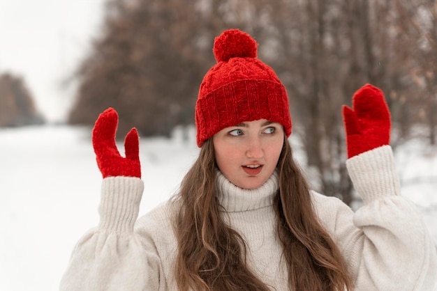 Portrait of beautiful blueeyed girl in knitted red hat and mittens and woolen sweater in winter park Ladies knitwear