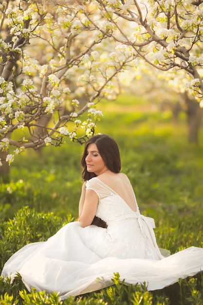 Portrait of beautiful bride in ivory wedding dress with long curly hair in spring blossom garden