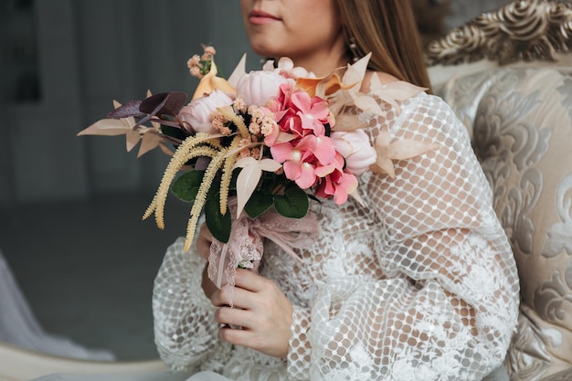 Portrait of a beautiful bride with a bouquet of hydrangea roses and feces in pastel orange color in her hands in a light interior