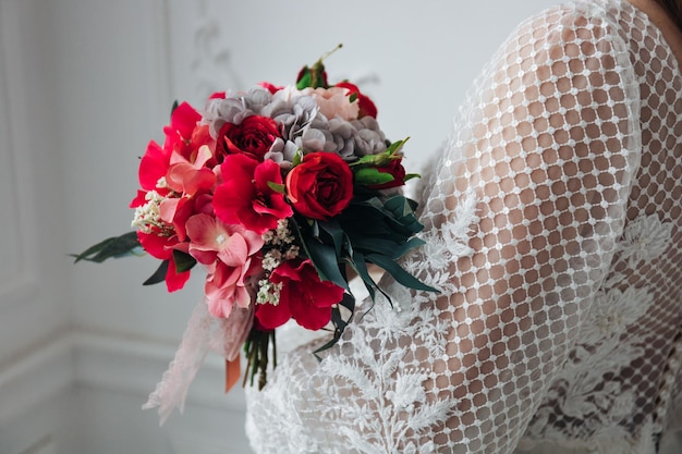 Portrait of a beautiful bride with a bouquet of hydrangeas and red roses in her hands in a light interior