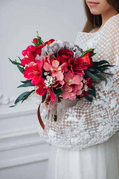 Portrait of a beautiful bride with a bouquet of hydrangeas and red roses in her hands in a light interior