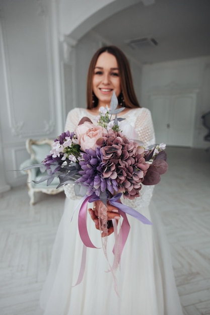 Portrait of a beautiful bride with a bouquet of purple hydrangea and peonies in her hands in a light interior