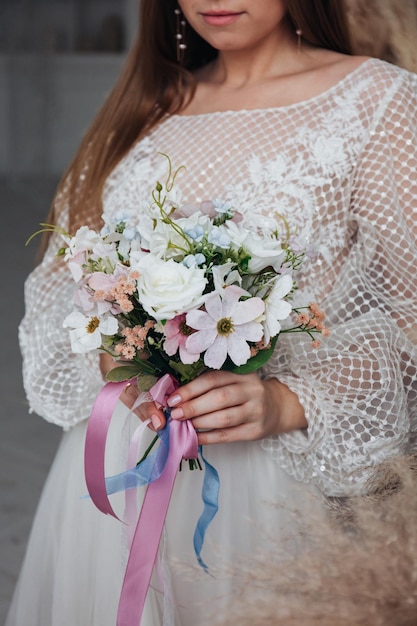 Portrait of a beautiful bride with a bouquet of white roses and pink daisies in her hands in a light interior