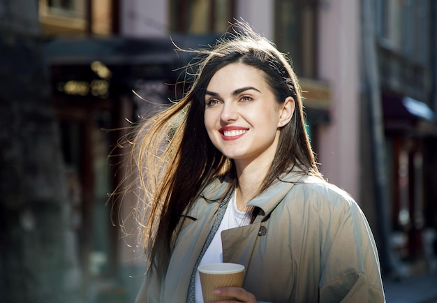 Portrait of beautiful brunette girl drinking coffe while standing at the spring sunny street