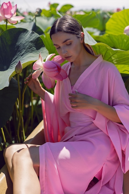 Portrait beautiful brunette woman in a pink dress is sitting on a boat among blooming lotuses on a lake in Astrakhan