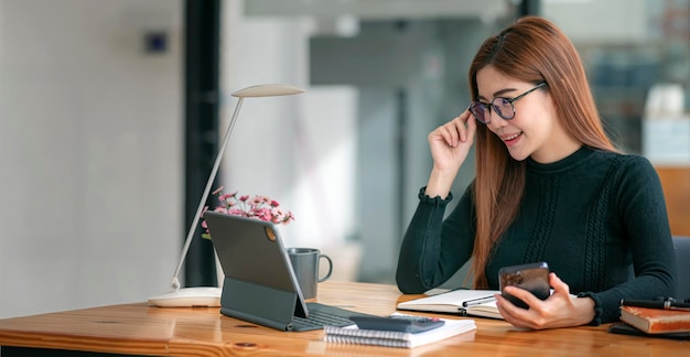 Portrait of the Beautiful Businesswoman using mobile phone and Working on a Laptop in Her Modern Office. Female Executive Uses Computer.