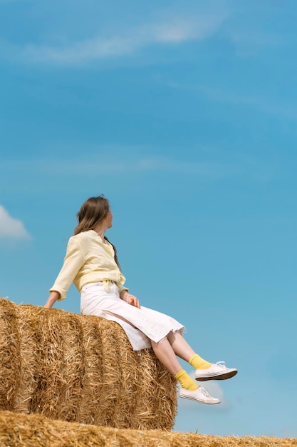 Portrait of beautiful caucasian woman sitting on haystack on farm on blue background Blue sky Harvesting