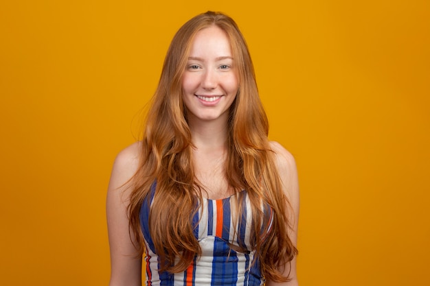 Portrait of beautiful cheerful redhead girl with flying hair smiling laughing  over yellow wall.