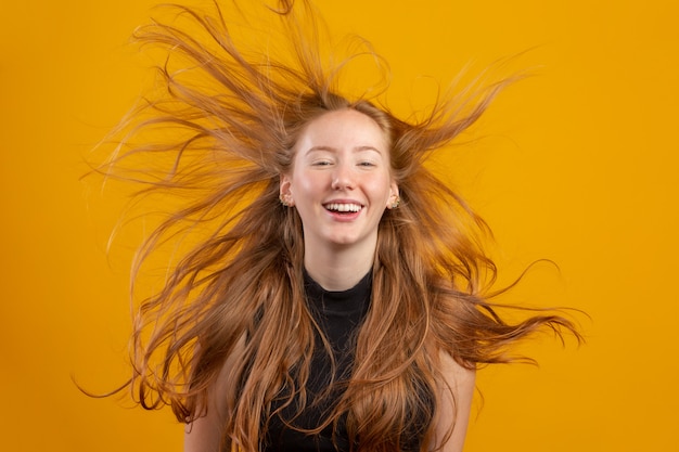 Portrait of beautiful cheerful redhead girl with flying hair smiling laughing  over yellow wall.