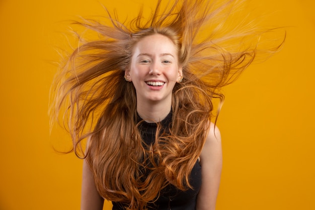 Portrait of beautiful cheerful redhead girl with flying hair smiling laughing  over yellow wall.