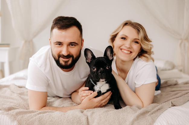 Portrait of beautiful couple and french dog in bed