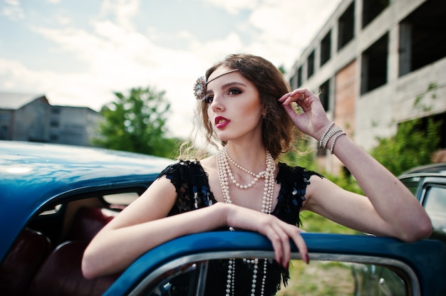 Portrait of beautiful curly fashion girl model with bright makeup in retro style leaned on a vintage car door.