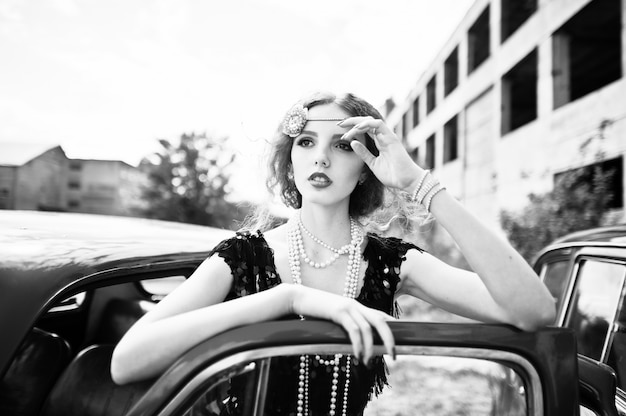 Portrait of beautiful curly fashion girl model with bright makeup in retro style leaned on a vintage car door.