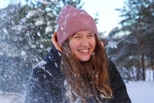 Portrait of a beautiful cute girl in the park or forest outdoors woman having fun laughing smiling at the nature teenager in warm cloth Blizzard and snow snowflakes falling down