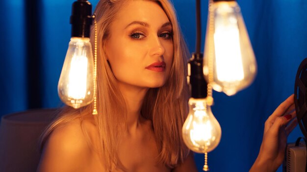 Photo portrait of a beautiful european girl a woman stands near a wall surrounded by edison's light bulbs