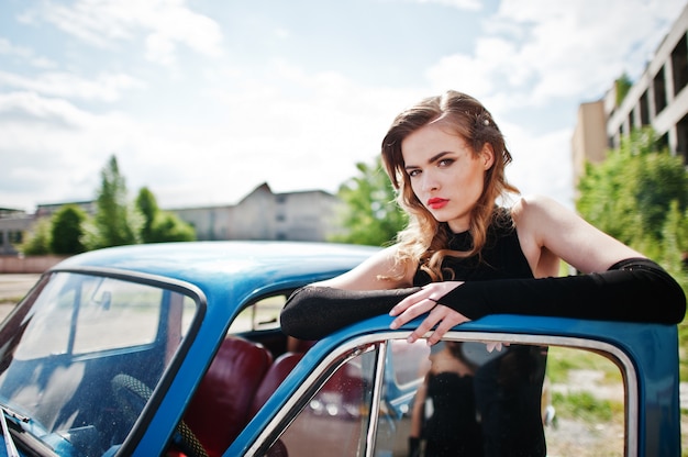 Portrait of beautiful fashion girl model with bright makeup in retro style leaned on a vintage car door.