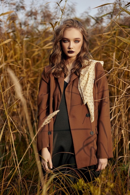 Portrait of a beautiful fashion woman in a thicket of autumn grass