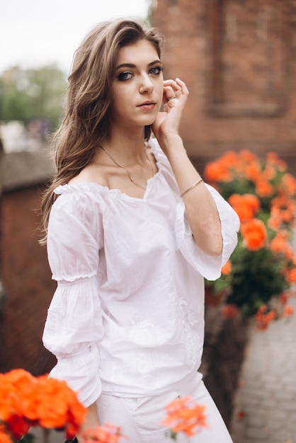 Portrait of a beautiful girl dressed in white and standing near the flowers