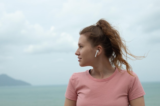 Portrait of a beautiful girl in earphones on the natural background of ocean or sea in the mountain