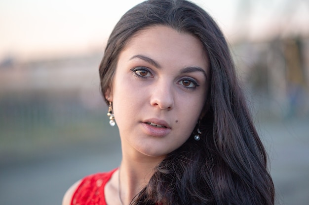 Portrait of a beautiful girl. Gorgeous brunette girl, portrait in soft evening light. Portrait of a young beautiful girl with long dark hair and in a red dress.