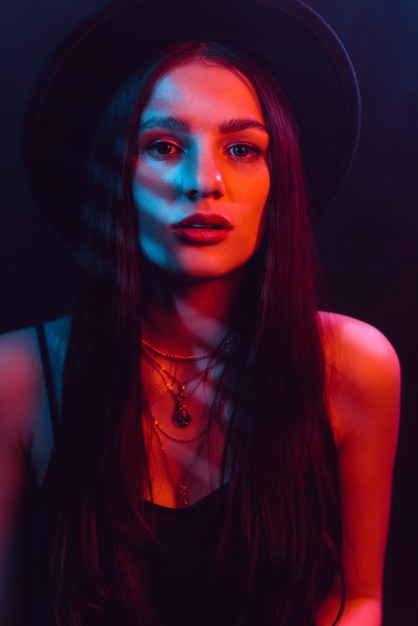 Portrait of beautiful girl in hat with red and blue neon light on black background