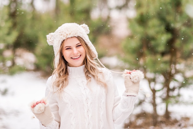 Portrait of a beautiful girl in light clothes in a winter forest. The girl smiles and enjoys the snow.