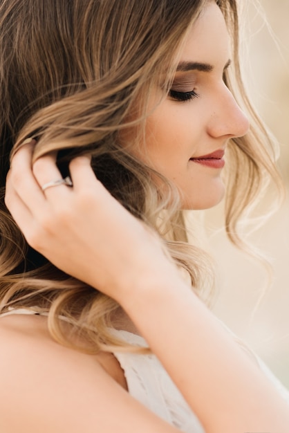 Portrait of a beautiful girl in a white dress with hair and makeup on the background of the sea