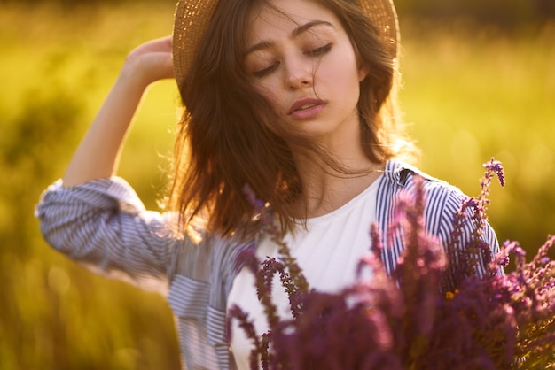 Portrait of a beautiful girl with a bouquet of lavender. Sunset light and beautiful sensuality. The girl is enjoying the moment