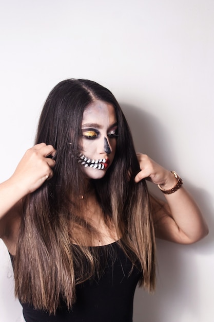 Portrait of a beautiful girl with Halloween makeup combing her hair on white background.