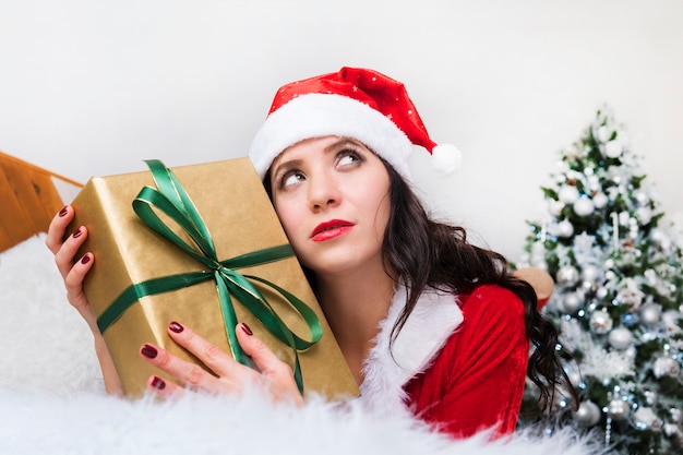 Portrait beautiful girl with long hair with box present and christmas hat. Thoughtful face girl. Dream of a good Christmas gift. Girl thinks. new year's dreams and hopes.