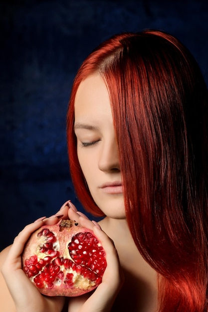 Portrait of beautiful girl with red hair and pomegranate fruit on the background of blue wall different poses