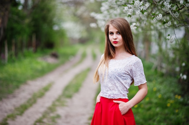 Portrait of beautiful girl with red lips at spring blossom garden, wear on red dress and white blouse.