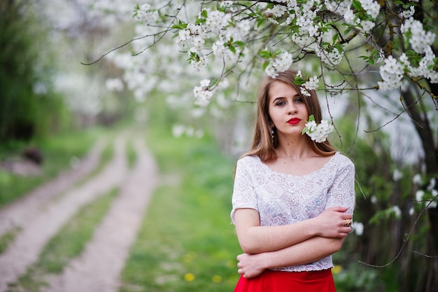 Portrait of beautiful girl with red lips at spring blossom garden wear on red dress and white blouse