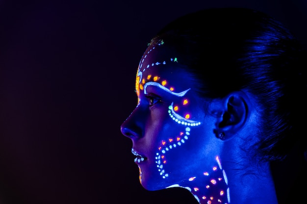 Portrait of beautiful girl with ultraviolet paint on her face. Girl with neon make-up in color light.