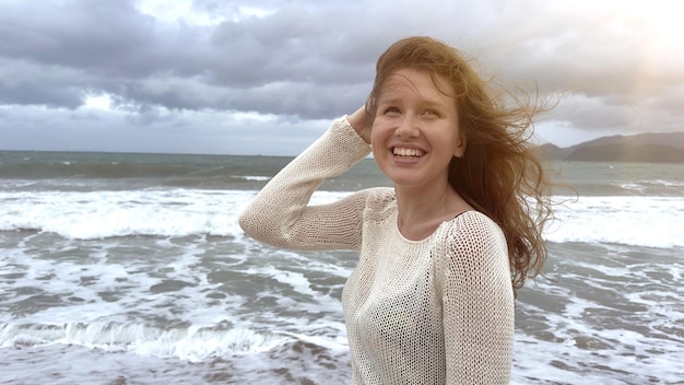 Portrait of beautiful girl young happy positive cheerful joyful woman enjoying vacation on sea ocean walking on summer beach in tropical country smiling having fun laughing in knitted sweater