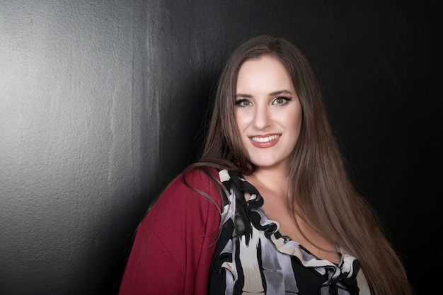 Portrait of a beautiful happy brunette smiling woman with long hair Cropped photo of plus size attractive model posing on black background with charming smile studio shot Space for text Smiling