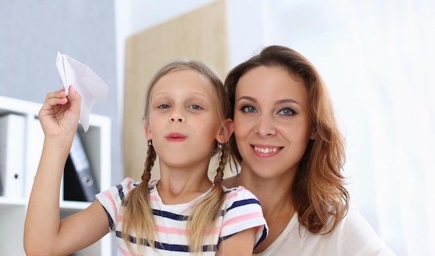 Portrait of beautiful happy mom with daughter are holding paper airplane